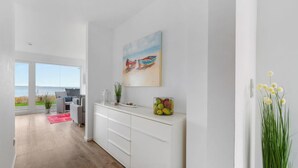 Eine moderne Küche mit weißen Schränken, einem Gemälde von Booten und Meerblick durch große Fenster.