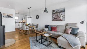 A modern living room with a grey sofa, a coffee table, and a dining area with a wooden table and chairs.