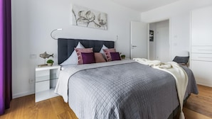 A modern bedroom with a bed, bedside tables, a nightstand, a headboard, a wall art piece, and a door.
