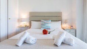 Un lit bien fait, avec du linge de lit blanc, deux serviettes enroulées, un coussin décoratif et deux lampes de chevet posées sur les tables de nuit.