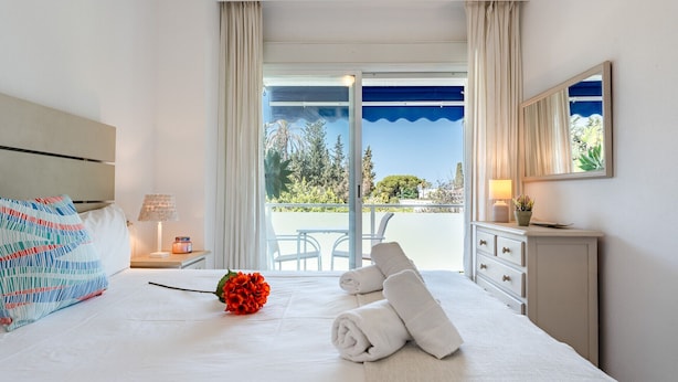 Une chambre d’hôtel avec un lit, une table de chevet, une lampe, une plante en pot et une vue sur l’extérieur.