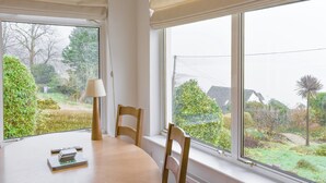 A dining area with a table, chairs, and a window with a view of a garden and houses.