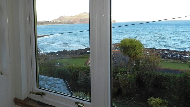 A window with a view of a coastal landscape, including a body of water and distant hills.