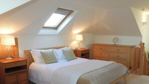 A bedroom with a skylight, a bed with white bedding, two bedside tables with lamps, a wooden dresser, and a chair.