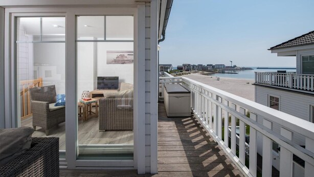 Un balcon doté de meubles en osier, d’un téléviseur et offrant une vue sur la plage et l’océan.