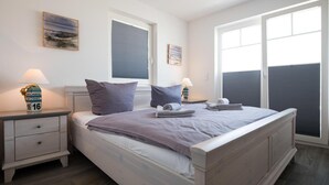 Une chambre à coucher comprenant un lit, deux tables de chevet, une commode, une fenêtre et une vue sur l’extérieur.