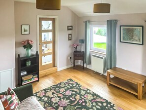 A room with a wooden floor, a bed, a bench, a desk with a lamp, a radiator, and a window with curtains.