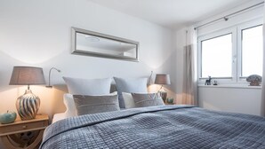 A bedroom with a bed, two bedside tables with lamps, a window with curtains, and a mirror on the wall.