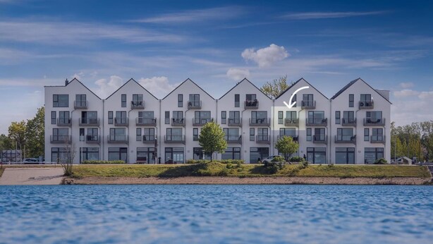 A modern multi-story residential building with balconies, located near a body of water.