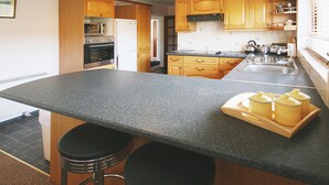 A kitchen with a granite countertop, wooden cabinets, a microwave, a refrigerator, a stove, and a sink. There are three stools at the counter. - 3 bedroom accommodation in Laide (Laide)