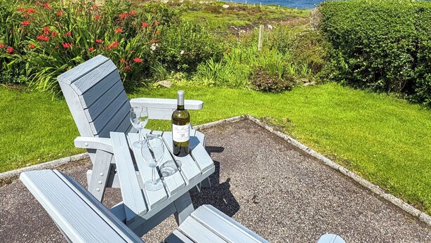 A wooden bench with a bottle of wine and glasses, set on a gravel path with a view of the sea and hills. - 3 bedroom accommodation in Laide (Laide)