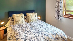 A neatly made bed with floral bedding, two bedside lamps, and a window with a view of greenery. - 3 bedroom accommodation in Laide (Laide)