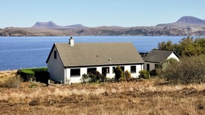 A house with a sloped roof, a chimney, and a view of a lake and mountains in the background. - 3 bedroom accommodation in Laide (Laide)