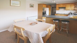 A dining area with a table set for four, wooden chairs, and a kitchen area with wooden cabinets and a countertop. - 3 bedroom accommodation in Laide (Laide)