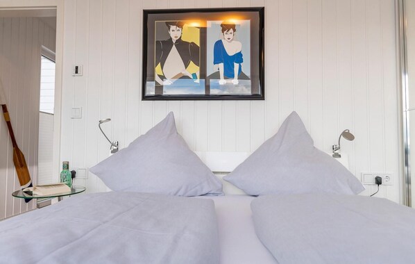 Habitación de hotel con una cama, dos lámparas de noche, una obra de arte enmarcada sobre la cama y una pala de madera apoyada en la pared.