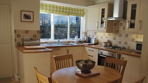 A kitchen with a dining table, chairs, a window with a view, and various kitchen appliances. - A charming, contemporary Lakeland cottage in the very heart of Ambleside. (Ambleside)