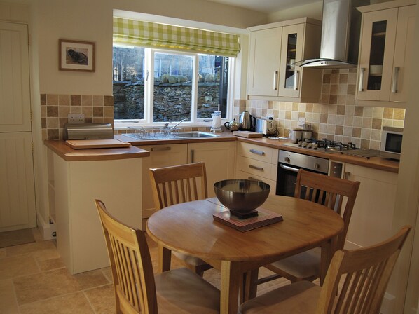 A kitchen with a dining table, chairs, a window with a view, and various kitchen appliances. - A charming, contemporary Lakeland cottage in the very heart of Ambleside. (Ambleside)