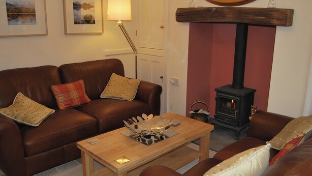 A living room with a brown leather sofa, a wooden coffee table, a fireplace, and framed pictures on the wall. - A charming, contemporary Lakeland cottage in the very heart of Ambleside. (Ambleside)