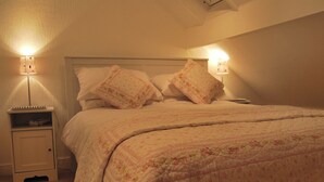 A neatly made bed with a floral quilt, two bedside lamps, and a nightstand with a lamp and a book. - A charming, contemporary Lakeland cottage in the very heart of Ambleside. (Ambleside)