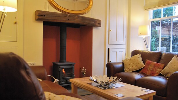 A living room with a fireplace, leather sofa, wooden coffee table, and a mirror on the wall. - A charming, contemporary Lakeland cottage in the very heart of Ambleside. (Ambleside)