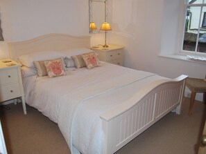 A neatly arranged bedroom with a bed, bedside tables, a lamp, a chair, and a window. - A charming, contemporary Lakeland cottage in the very heart of Ambleside. (Ambleside)