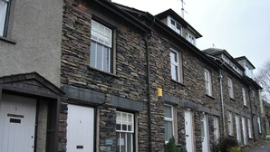 A row of stone houses with white doors, each marked with a number and name, and a small garden area with plants. - A charming, contemporary Lakeland cottage in the very heart of Ambleside. (Ambleside)
