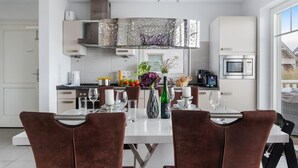 Une cuisine moderne avec des meubles blancs, des appareils en acier inoxydable et un coin repas comprenant des chaises marron et une table blanche dressée pour deux personnes.