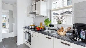 Une cuisine moderne avec des armoires blanches, un évier en acier inoxydable et un four encastré. Une fenêtre offre une vue sur l’extérieur, et une plante est posée sur le plan de travail.