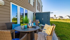 An outdoor patio with wicker furniture, a round table with a fruit basket, and a blue outdoor lamp. - Nice apartment in Olpenitz with sauna (Olpenitz)