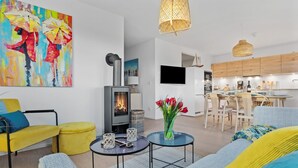 A modern living room with a fireplace, yellow and blue furniture, a dining area, and a kitchen with wooden cabinets. - Nice apartment in Olpenitz with sauna (Olpenitz)