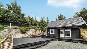 A cabin with a deck, outdoor seating, and a view of the surrounding forest.