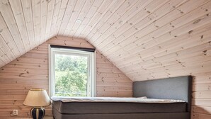 A bedroom with a sloped ceiling, a bed, a window, and a lamp.
