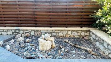 A stone wall with a wooden fence, a gravel area with rocks and logs, and a plant with white flowers.