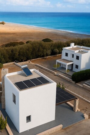 A modern building with solar panels on the roof, situated near a beach with a clear view of the ocean. - Villa Solmar Rhodes. Seafront Escape: Luxurious Villa on Lachania Beach. (Lachania, Rhodes Island)