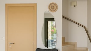 Une pièce avec une porte en bois, une chaise avec un coussin, un miroir et un escalier.