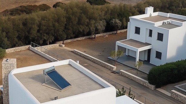 Un bâtiment moderne doté d’un toit plat et d’un panneau solaire, offrant une vue sur une plage et la mer.