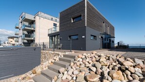 A modern building with a flat roof, large windows, and a stone pathway leading to the entrance. - Cozy home in Olpenitz with sauna (Olpenitz)