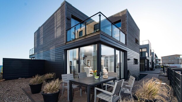 A modern two-story house with a glass conservatory, outdoor seating, and potted plants. - Cozy home in Olpenitz with sauna (Olpenitz)