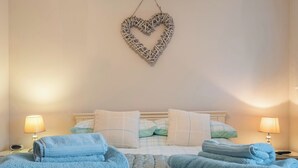 Una habitación de hotel con una cama, dos lámparas de noche, una decoración en forma de corazón en la pared y toallas dobladas.