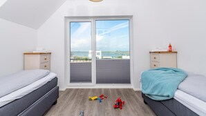 Un dormitorio con dos camas, vista al mar y un balcón con juguetes.
