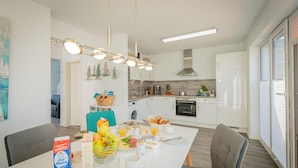 Cocina moderna con armarios blancos, una isla central con alimentos para el desayuno, horno empotrado y un ventanal grande.