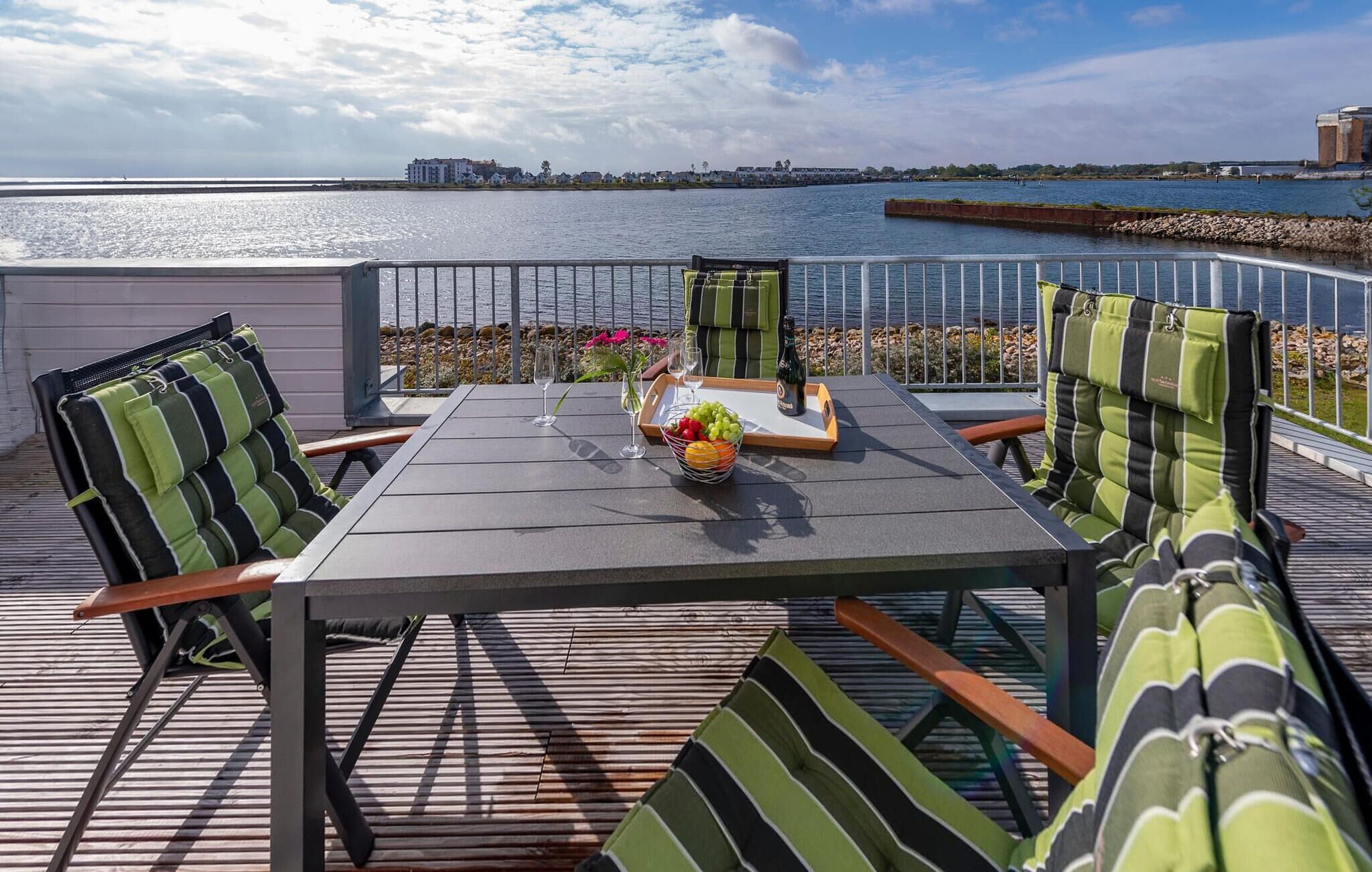Terraza con una mesa dispuesta para dos, con cojines a rayas, un frutero, copas de vino y una botella.