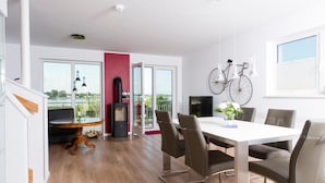 A modern dining area with a white table and leather chairs, a wood-burning stove, and a view of the outdoors through large windows. - Nice home in Olpenitz with sauna (Olpenitz)