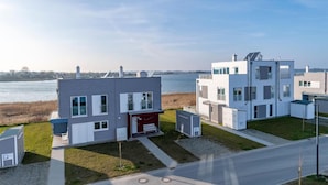 A modern residential complex with multiple two-story buildings, a small red house, and a view of a body of water. - Nice home in Olpenitz with sauna (Olpenitz)