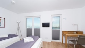 A modern hotel room with two beds, a desk, a chair, a TV, and large windows with a city view. - Nice home in Olpenitz with sauna (Olpenitz)