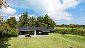 Une maison moderne avec un garage, une terrasse dotée de mobilier d’extérieur et une pelouse bien entretenue.