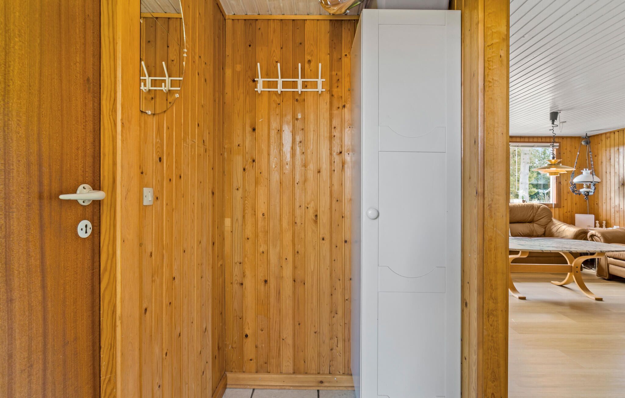 Un intérieur en bois avec une porte blanche, un porte-manteau et un coin repas comprenant une table et des chaises.