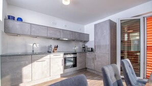 Una cocina moderna con armarios grises, horno empotrado y cafetera. En primer plano, hay dos sillas y una mesa.