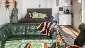 Ein kompakter Wohnraum mit einem dunkelgrünen Ledersofa, einem Bett mit gestreiften Kissen, einer kleinen Küchenzeile und einem Holz-Bediener.