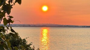 Ein Sonnenuntergang über einem Gewässer mit einer fernen Küstenlinie und Windkraftanlagen.